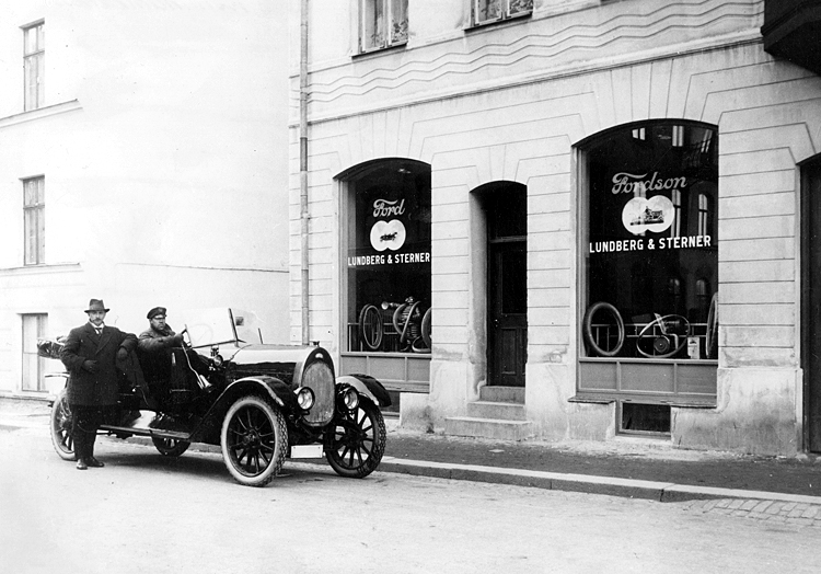 Svartvitt foto från 1910: bildelsaffären Lundberg & Sterner på Frejagatan 3, med en öppen bil och två män framför skyltfönstren.